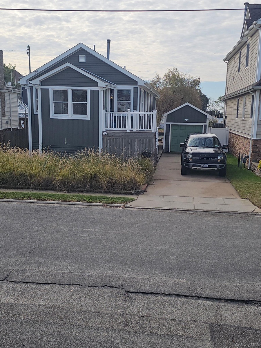 Dark-toned horizontal siding exterior featuring a front-facing wood deck with white railings, a detached garage, and a concrete driveway