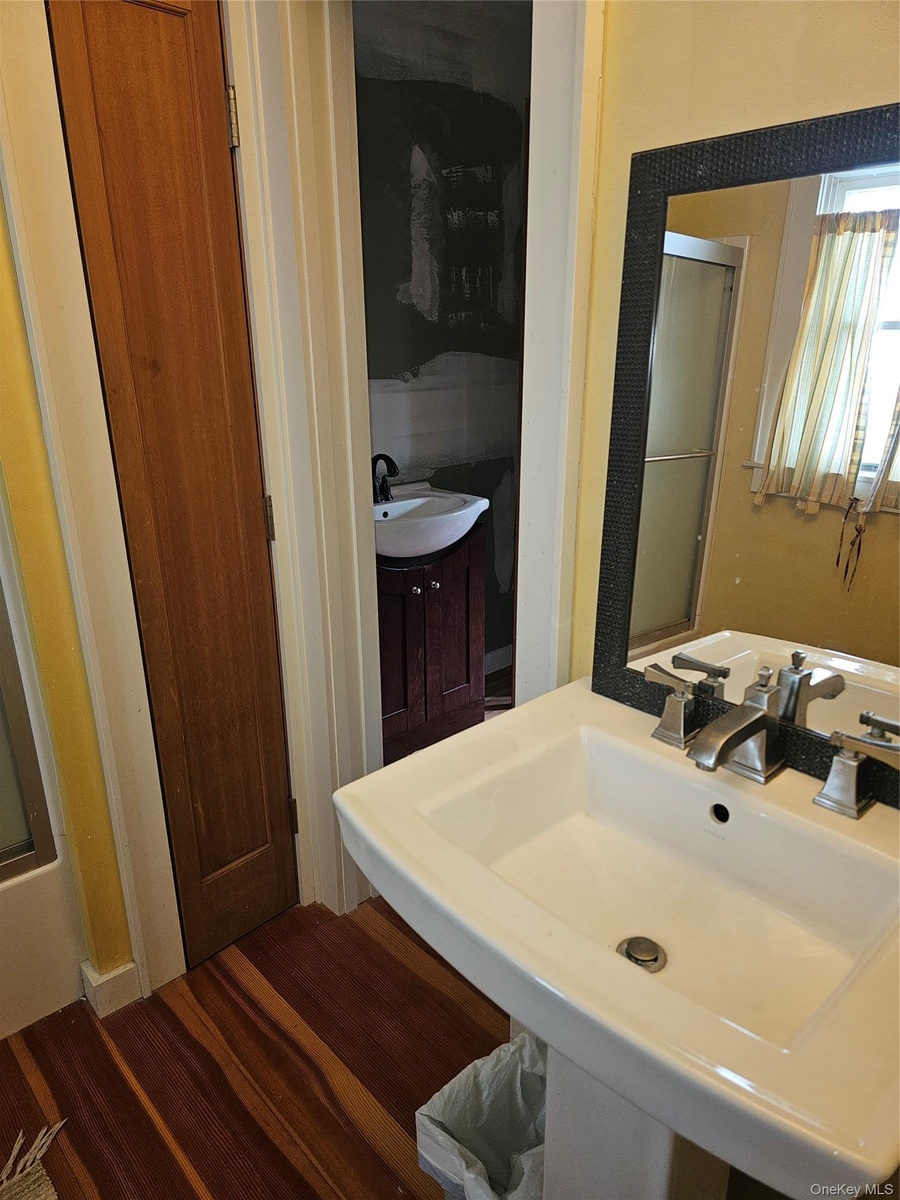 Pedestal sink with polished metal faucet, wood-finish flooring, and framed wall-mounted mirror