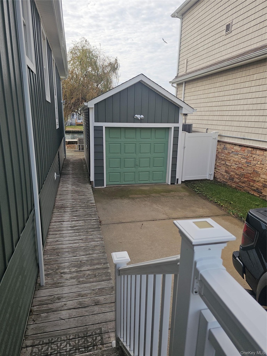 Detached garage featuring vertical siding, concrete driveway, and white vinyl privacy fencing