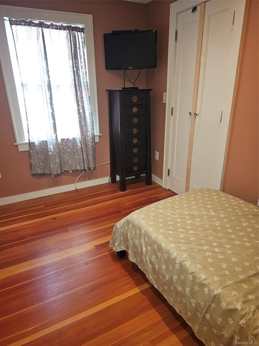 Natural wood-finish flooring, double-panel closet doors with hardware, and a window with white trim