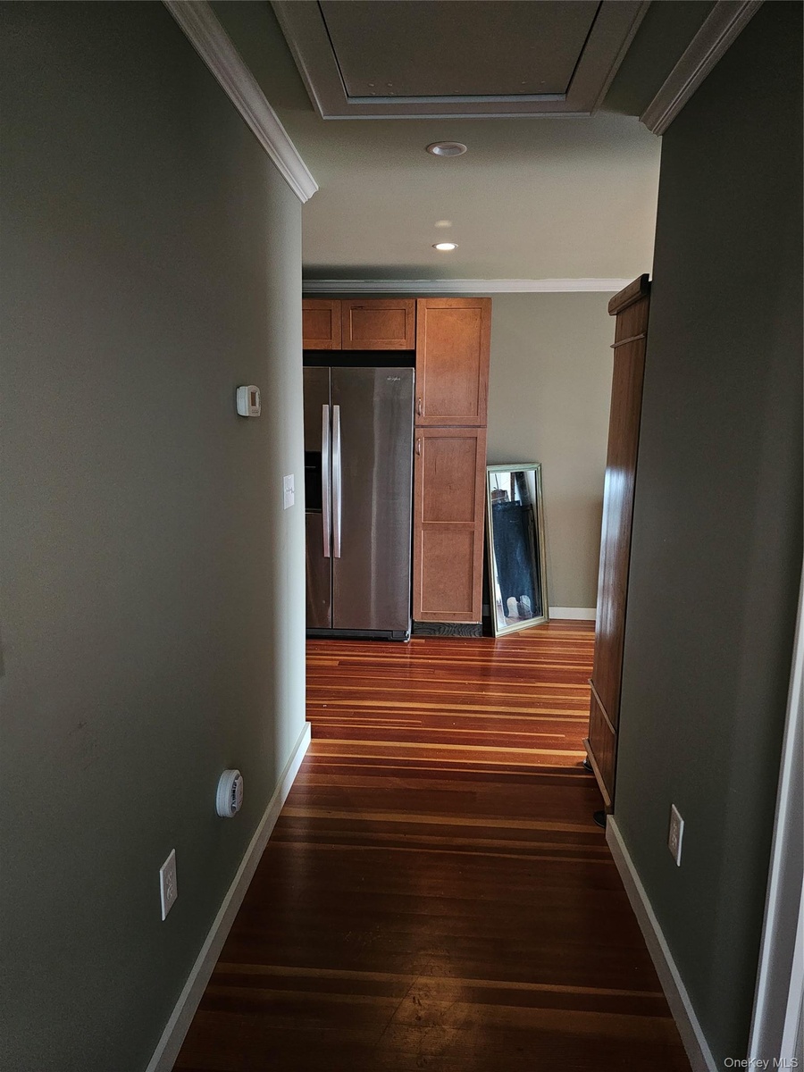 Wood-finish flooring, recessed lighting, crown molding, and wooden cabinetry with a stainless steel refrigerator