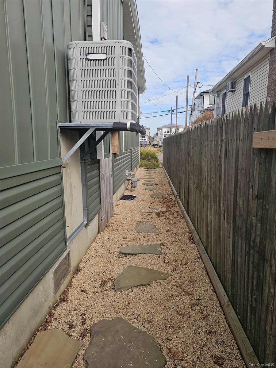 Side yard featuring a gravel path with integrated stone pavers, a tall wood-picket privacy fence, and a wall-mounted exterior HVAC unit