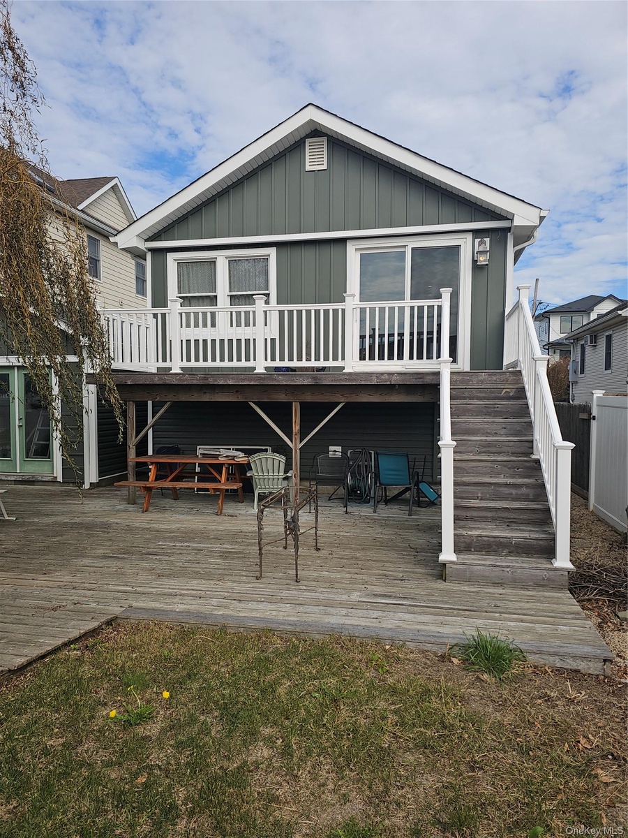 Exterior featuring board and batten siding, elevated deck with white railing, wood-surface patio, and staircase