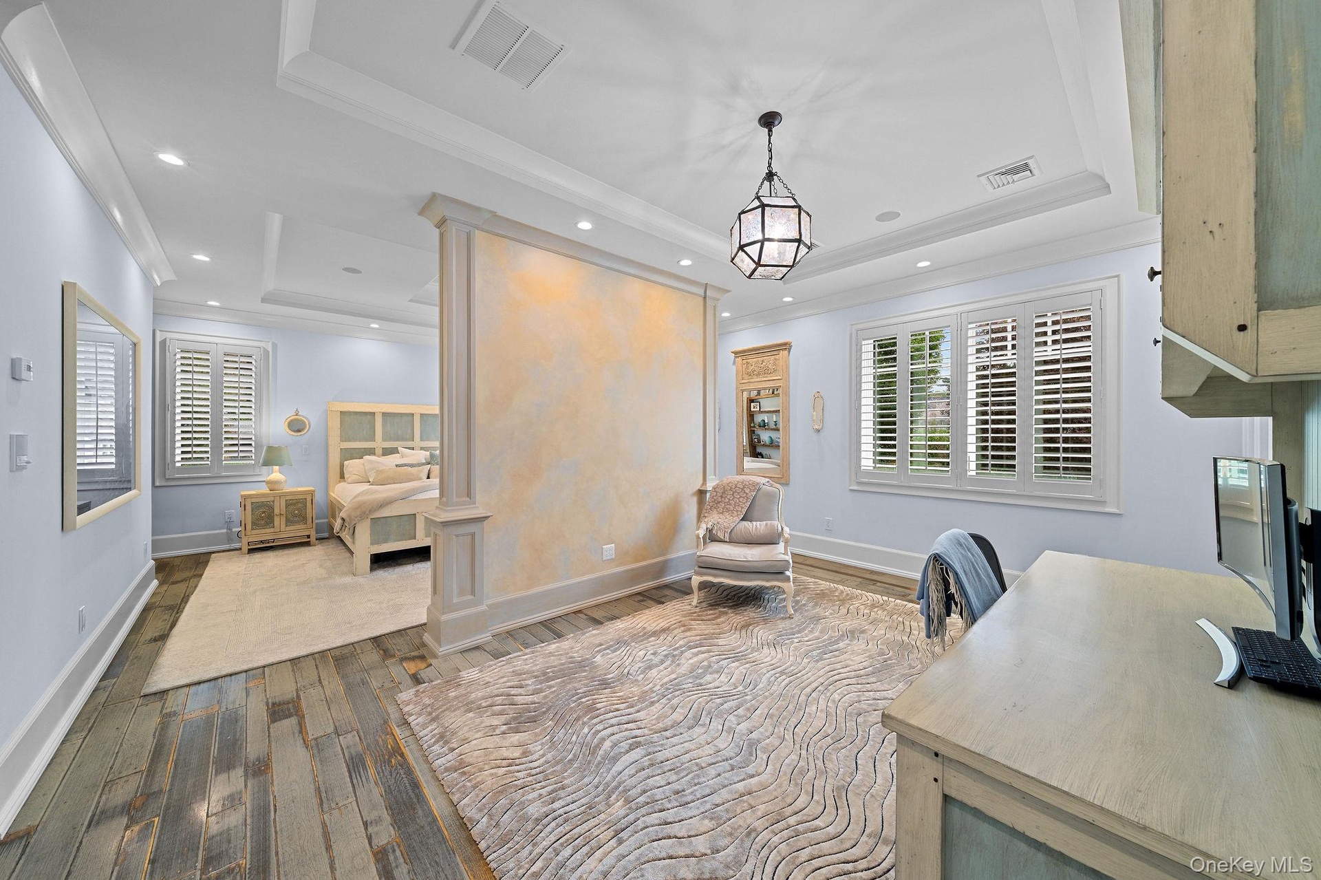 Tray ceilings with crown molding, custom partition wall with decorative finish, wood-finish flooring, recessed lighting, and plantation shutters