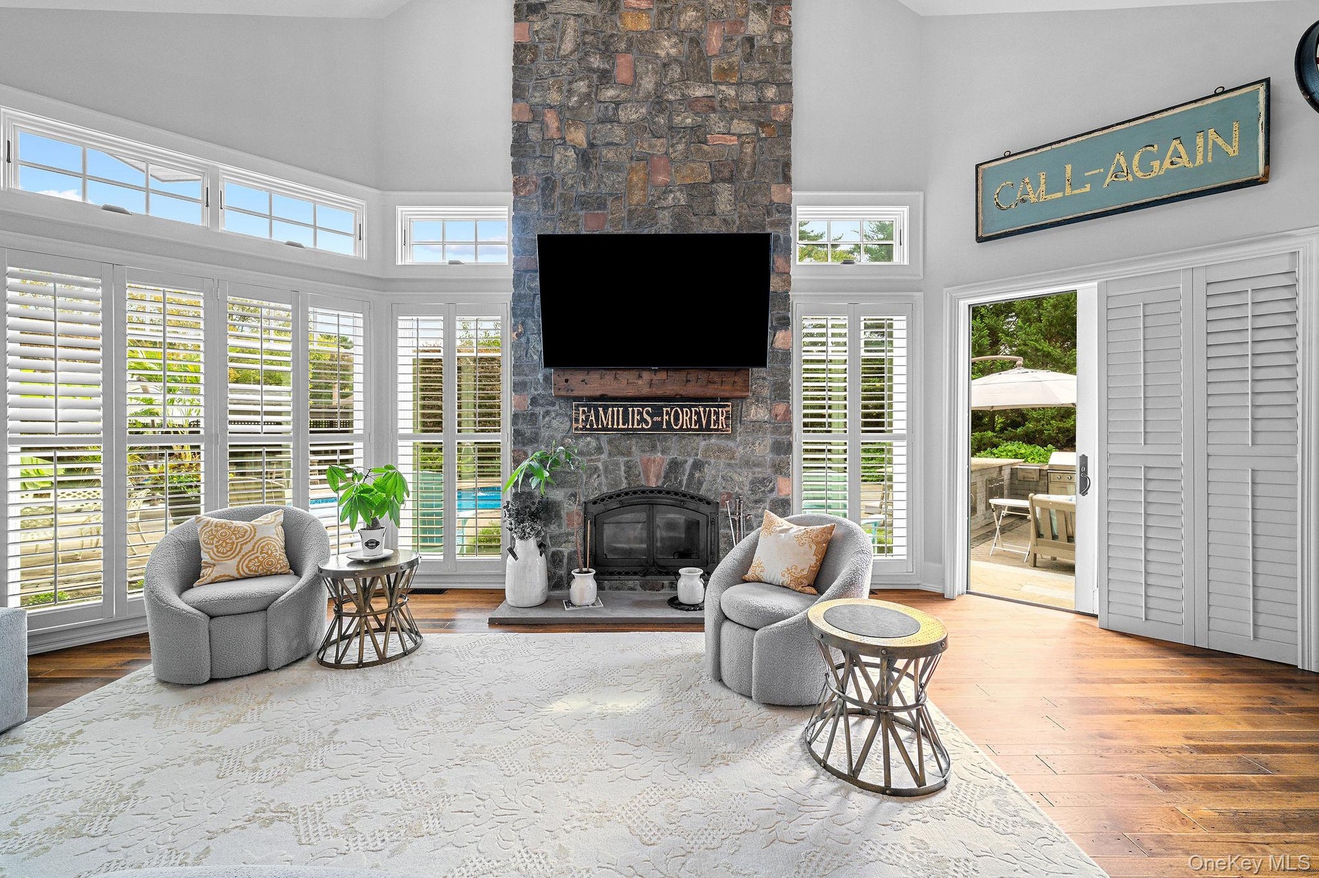 Vaulted ceiling, floor-to-ceiling stone fireplace with timber mantel, extensive window configuration with interior plantation shutters, and wood-finis