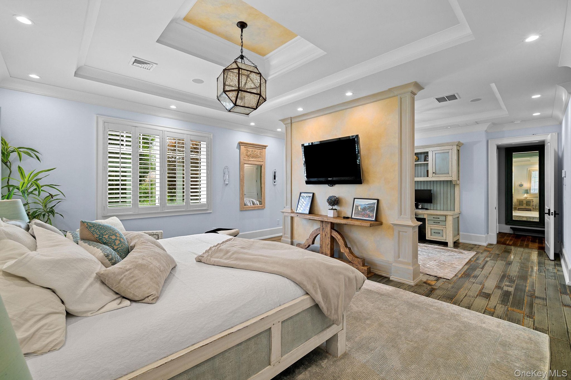 Tray ceiling with recessed lighting and decorative metallic finish, wood-finish flooring, plantation shutters, and central architectural partition wit