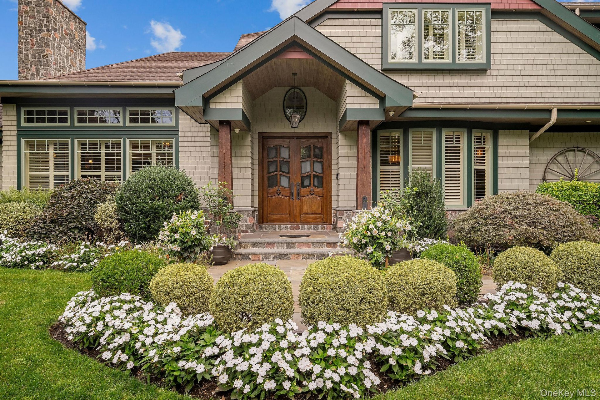 Craftsman-style exterior featuring shingle siding, a covered entryway with stone porch, custom wood double doors, and an exterior stone chimney