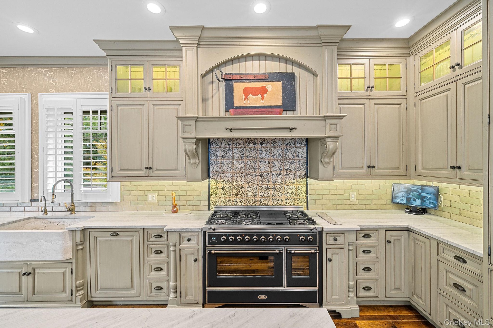 Custom-painted cabinetry featuring glass-front upper displays and a decorative hood enclosure, professional-grade dual-fuel range, farmhouse sink with