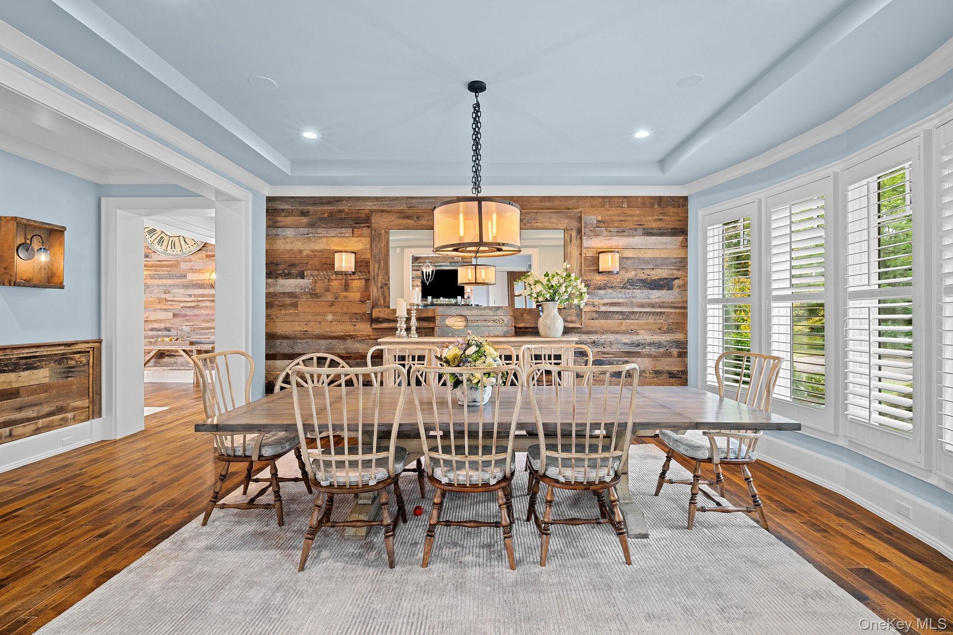 Dining area featuring wood-plank accent walls, tray ceiling, wood-finish flooring, and bay windows with plantation shutters