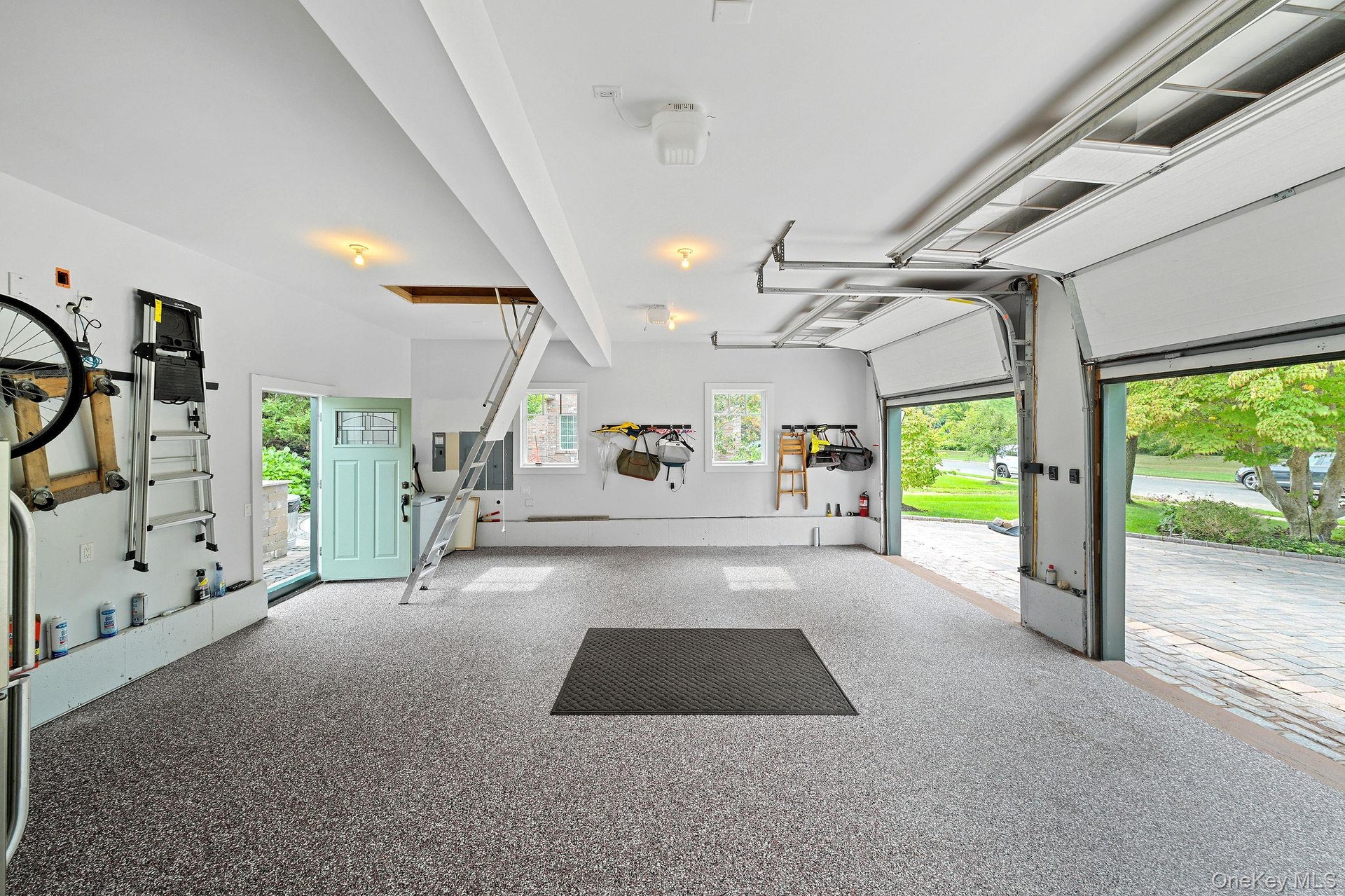 Multi-car garage featuring speckled epoxy flooring, overhead garage door system, integrated attic access ladder, and dual double-pane windows