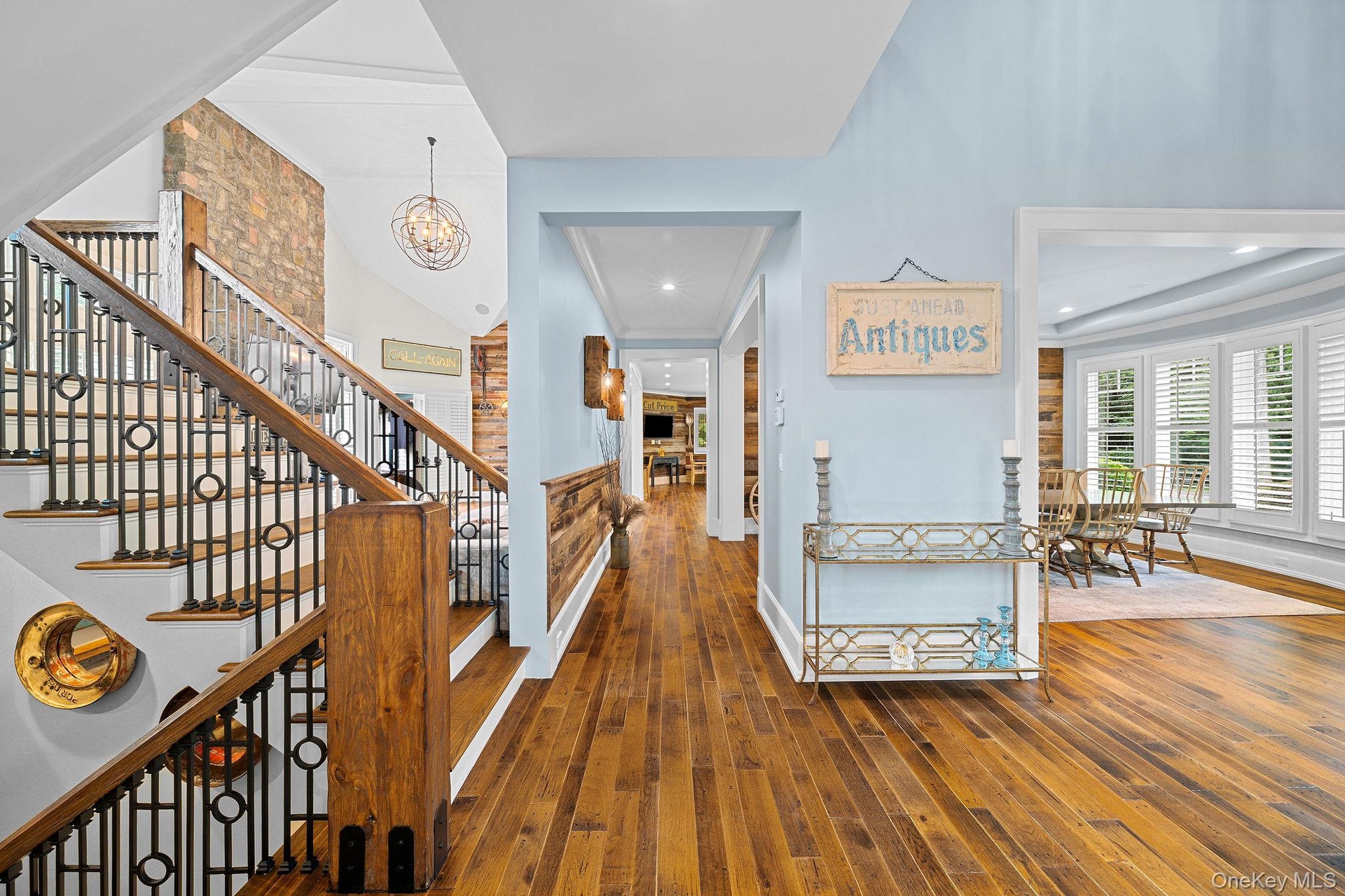 Interior featuring wood-finish flooring, a staircase with a metal railing and wood-tone newel post, an accent wall with stone masonry, horizontal wood
