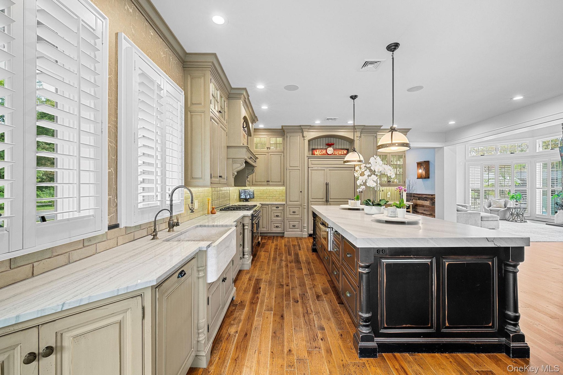 Kitchen featuring custom cabinetry, farmhouse-style sink, wood-finish flooring, stone-surfaced countertops, and a substantial center island