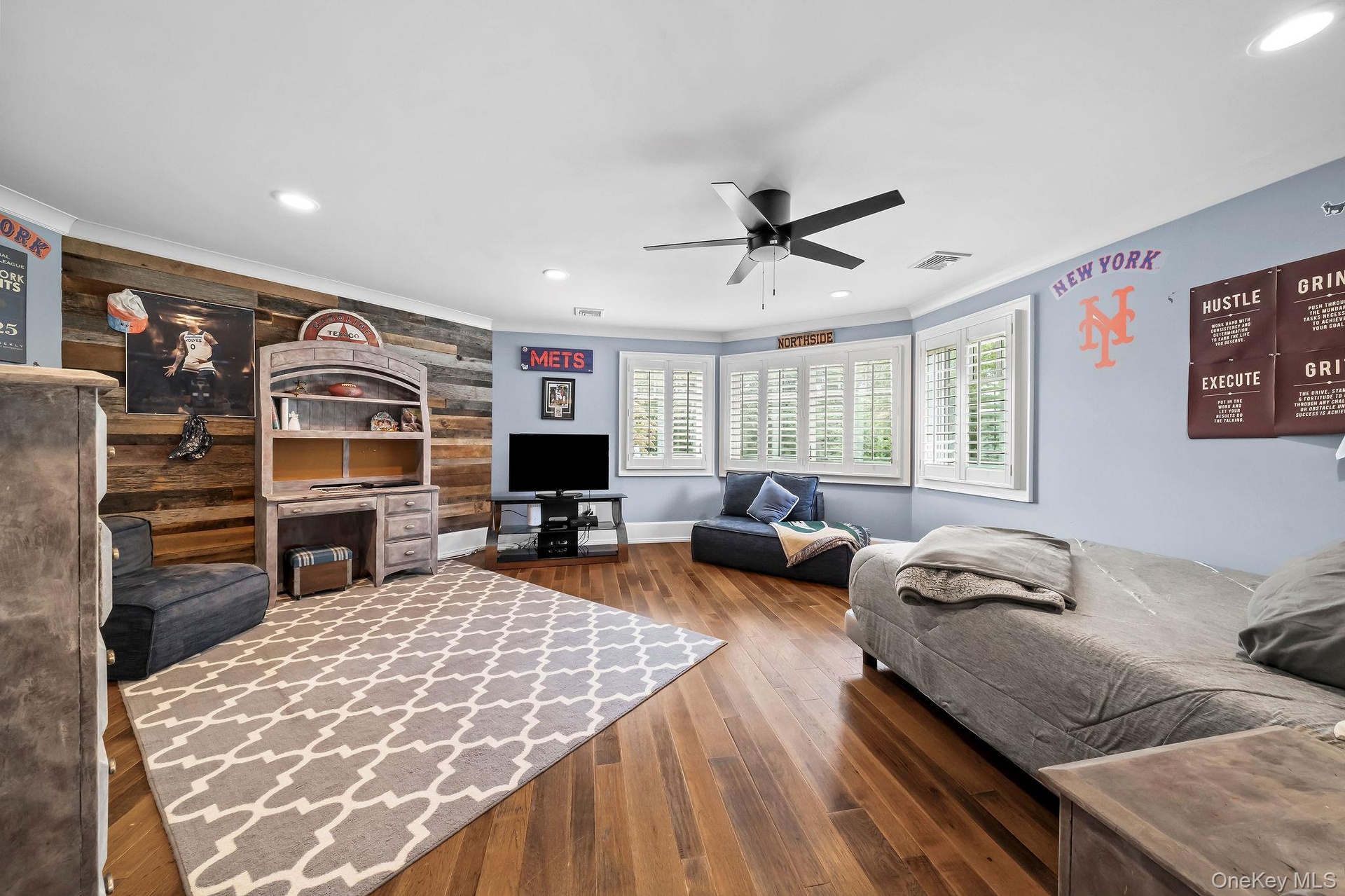 Wood-finish flooring, reclaimed wood-style plank accent wall, recessed lighting, matte black ceiling fan, and plantation shutters