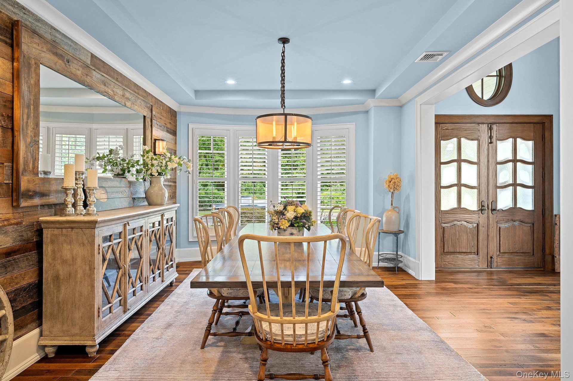 Dining area featuring wood-finish plank flooring, wood-paneled accent wall, tray ceiling with recessed lighting, bay windows with plantation shutters,