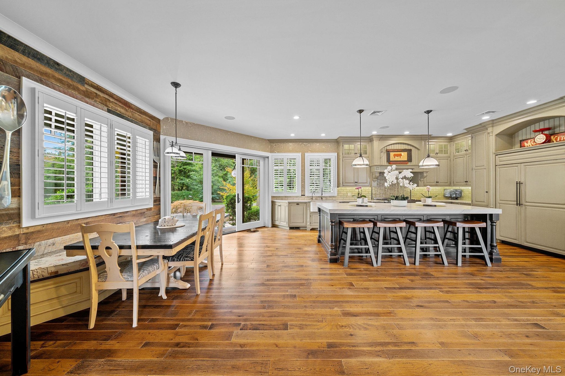 Kitchen featuring a large center island, wood-finish flooring, custom cabinetry, built-in panel-ready refrigerator, and reclaimed wood accent wall