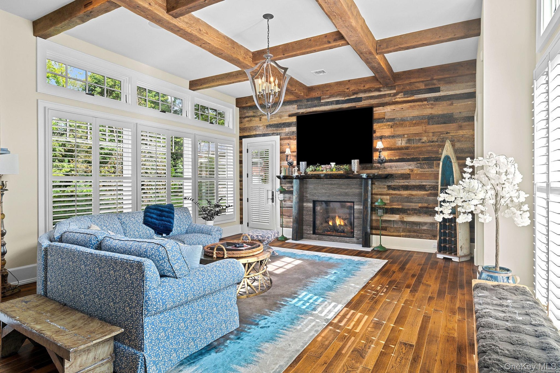 Living room featuring a reclaimed wood accent wall, stone-surround fireplace with a live-edge mantel, exposed timber ceiling beams, wood-finish floori