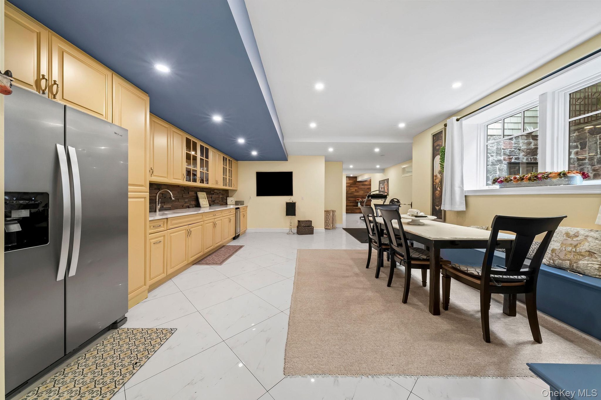 Kitchen featuring stainless steel refrigerator, light wood cabinetry, stone-texture backsplash, recessed lighting, and large-format tile flooring