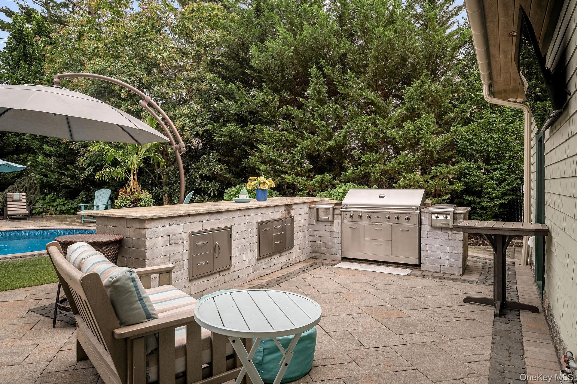 Outdoor kitchen featuring stone masonry, stainless steel built-in grill, stone-slab countertop, integrated storage cabinetry, and paver patio