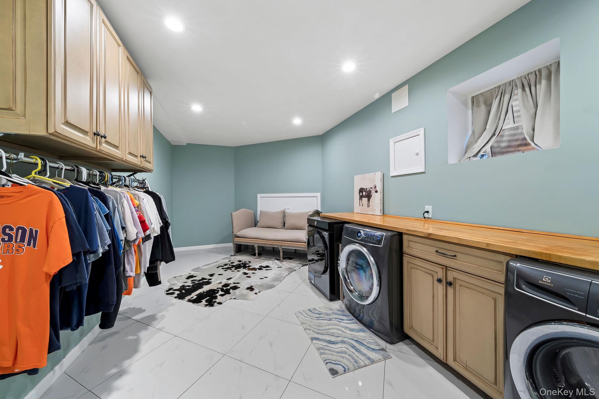 Dedicated laundry room featuring tile flooring, neutral wall-mounted cabinetry, an expansive wood-finish folding counter, and recessed lighting
