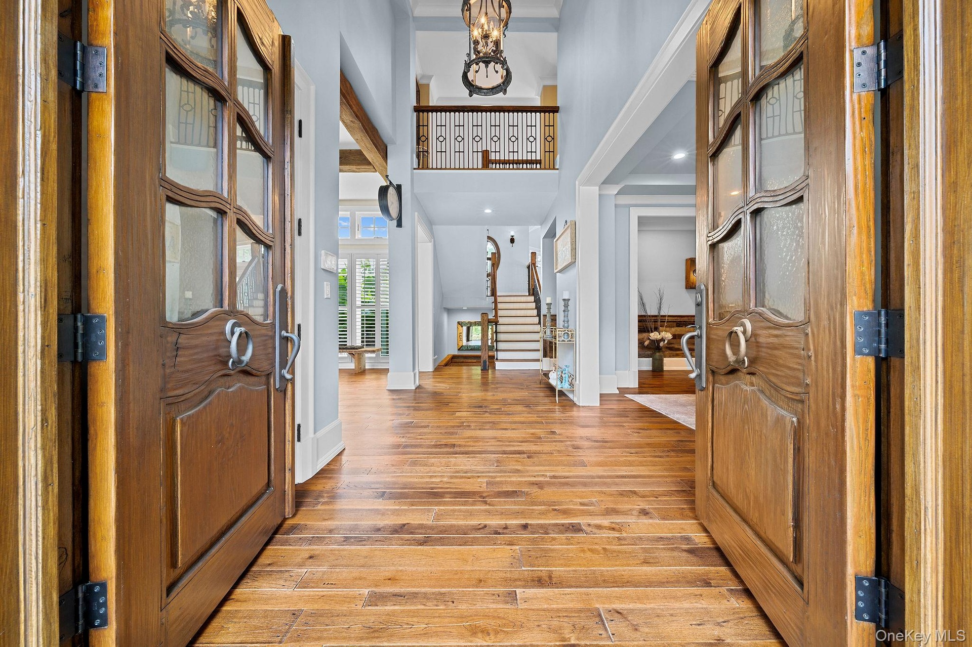 Double front doors featuring wood construction and glass inserts, wood-finish flooring, two-story ceiling height, intricate metal stair railing, and s