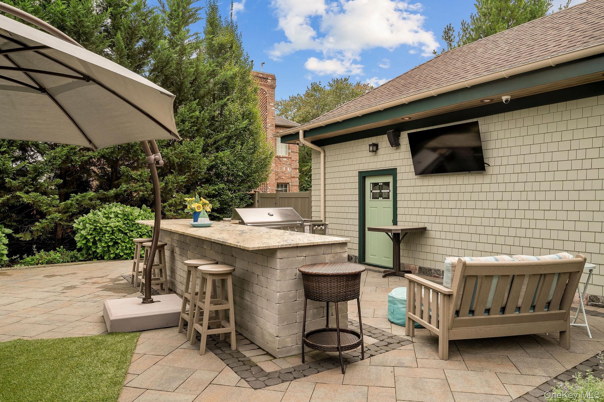 Outdoor patio featuring a stone-paver hardscape, built-in masonry grill island with a stone countertop, and exterior wall-mounted television