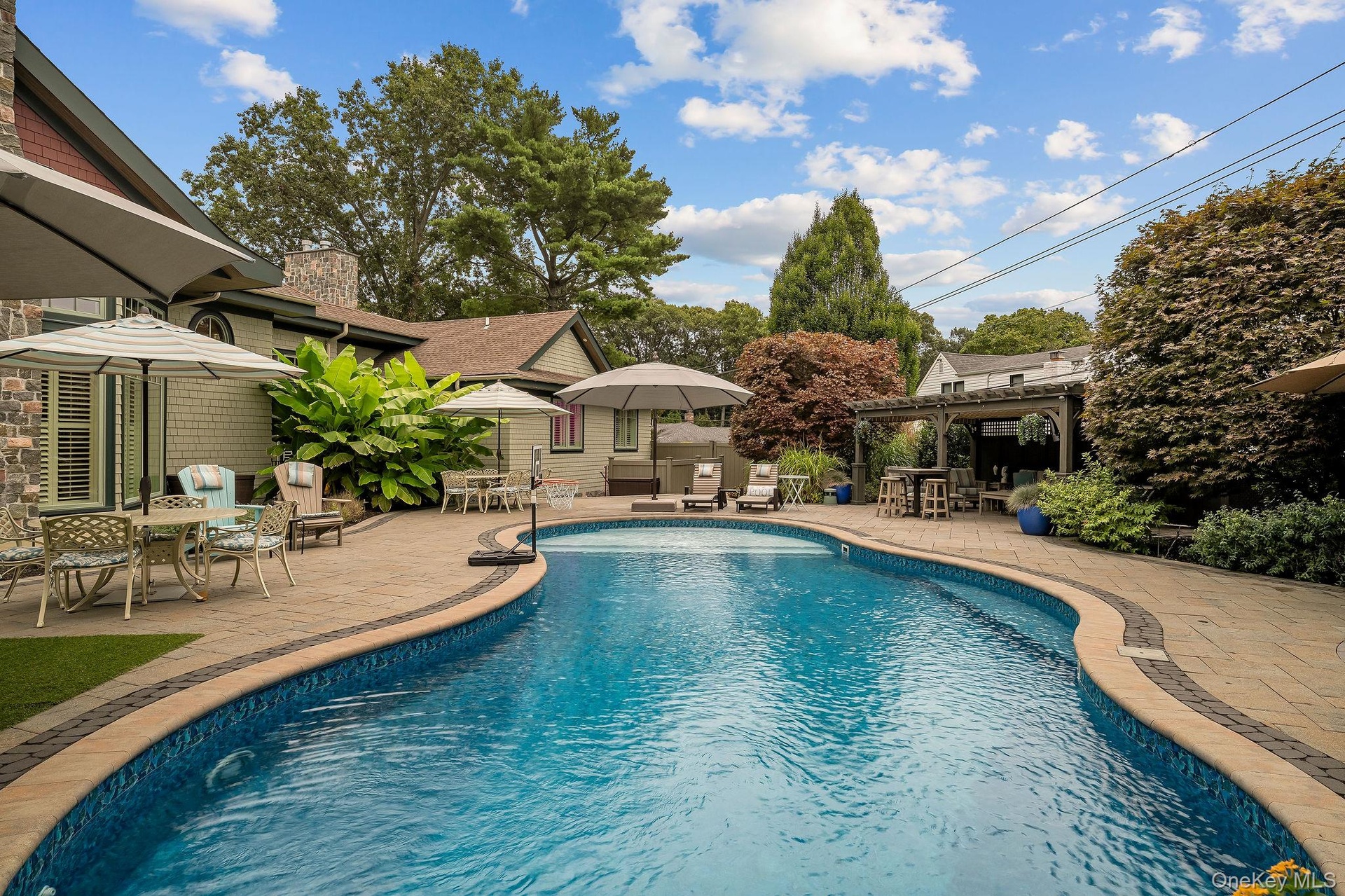 Curved in-ground swimming pool featuring stone-paver decking, a built-in pergola, and stone masonry exterior siding