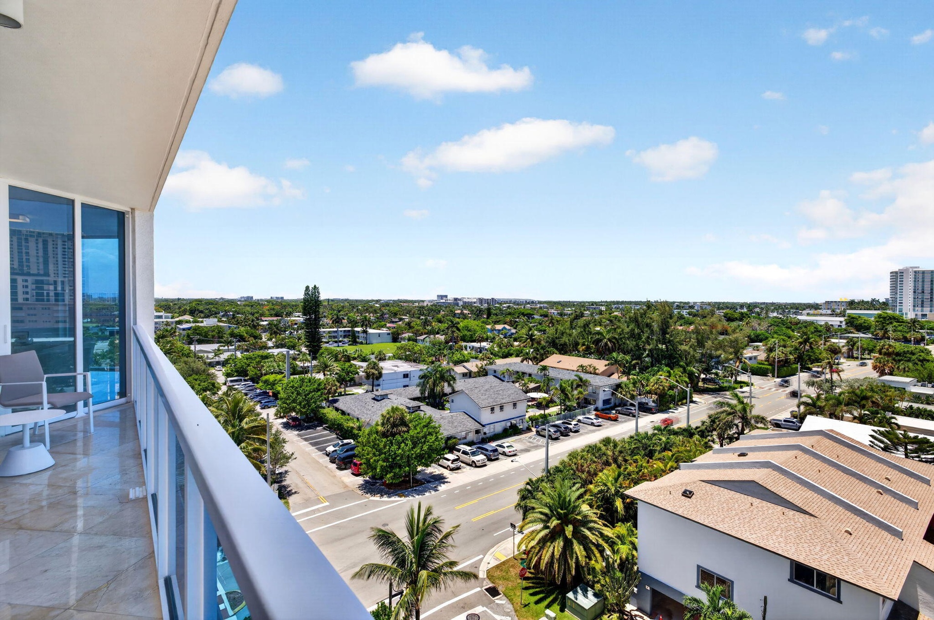 Expansive balcony with light-toned flooring, clear glass railing panels, and floor-to-ceiling windows