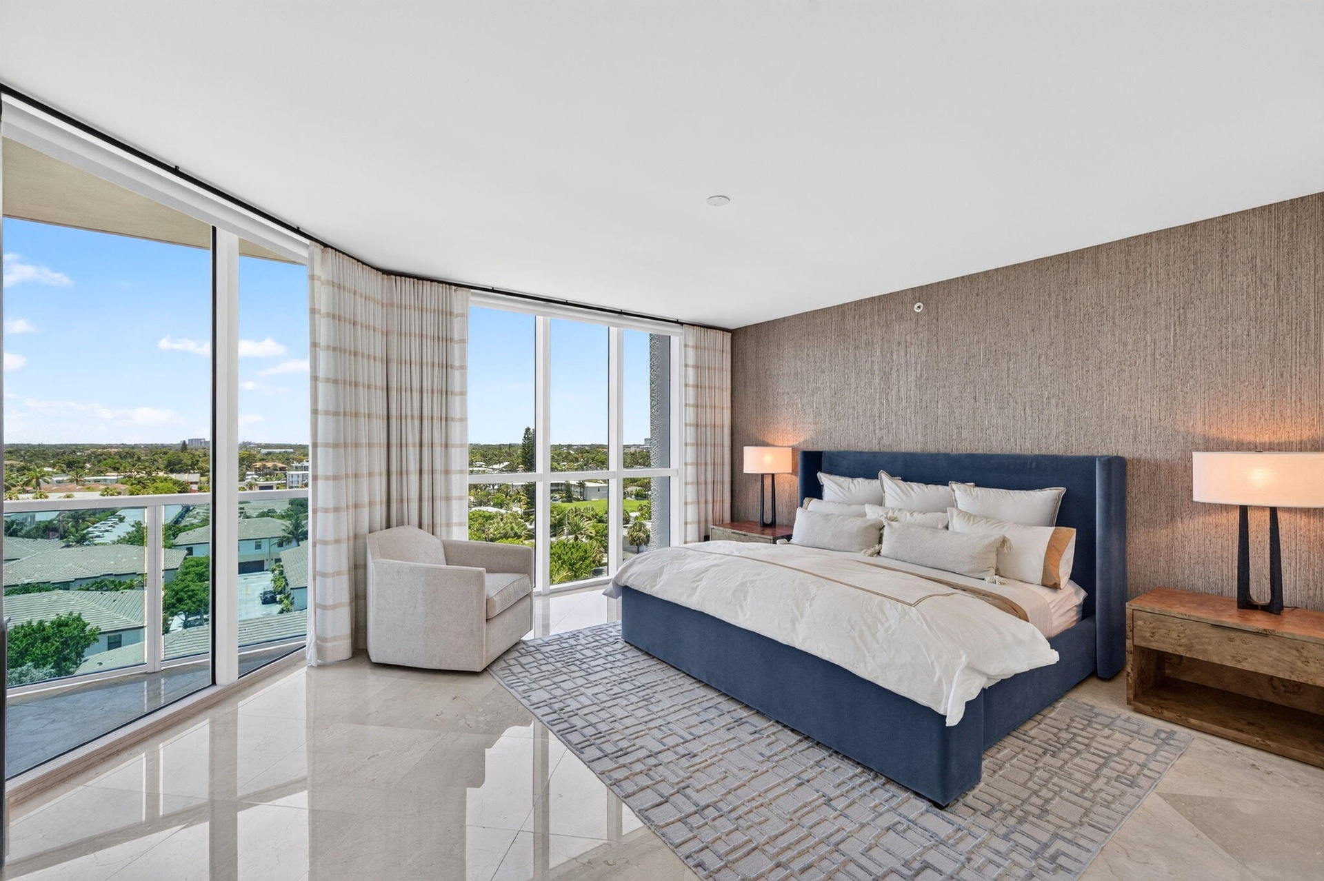 Expansive window wall, textured accent wall, polished marble flooring, recessed lighting, and balcony access