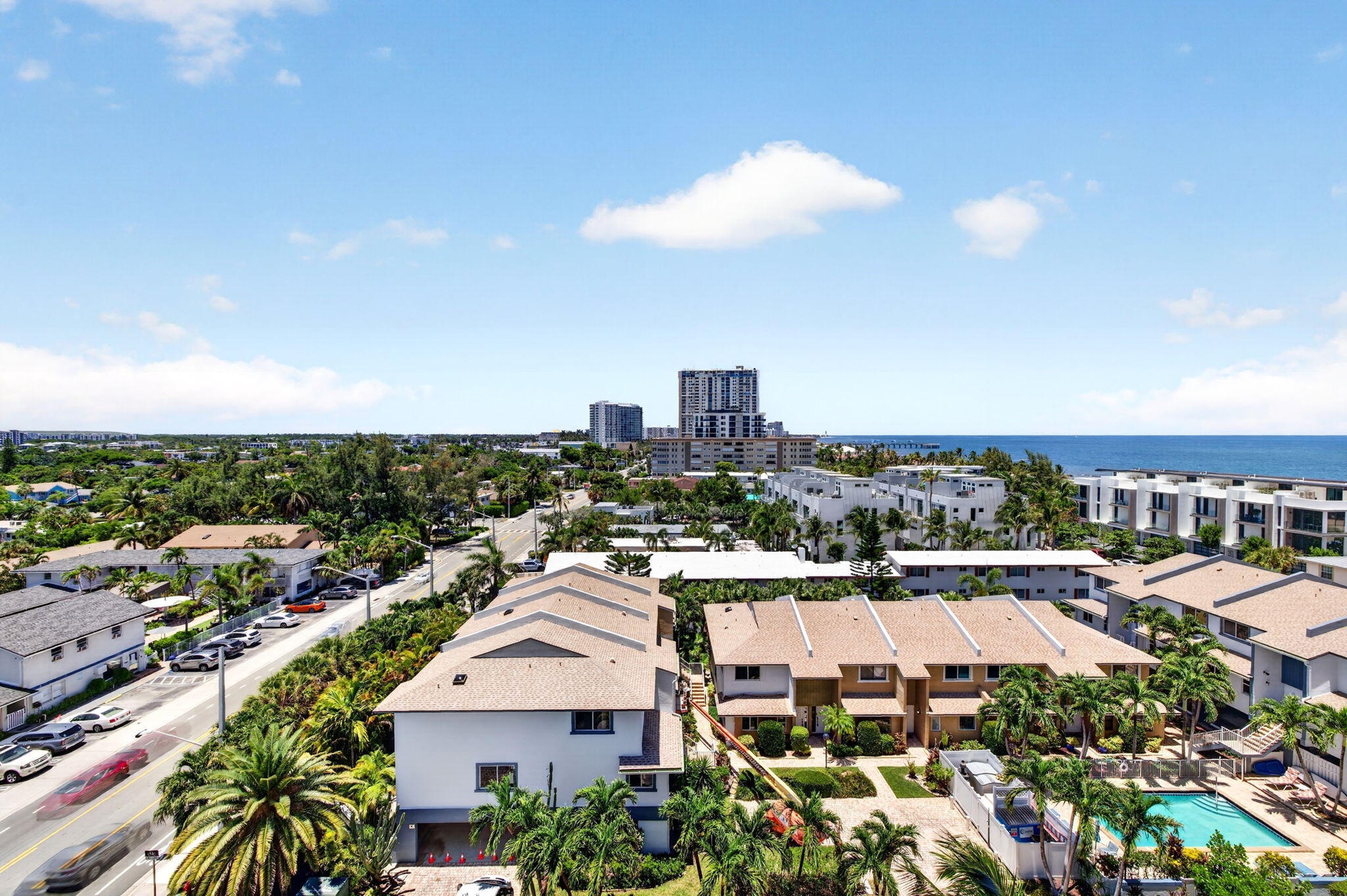 Aerial perspective showcasing the residential community with mature tropical landscaping, resort-style swimming pool, multi-unit architecture with tan