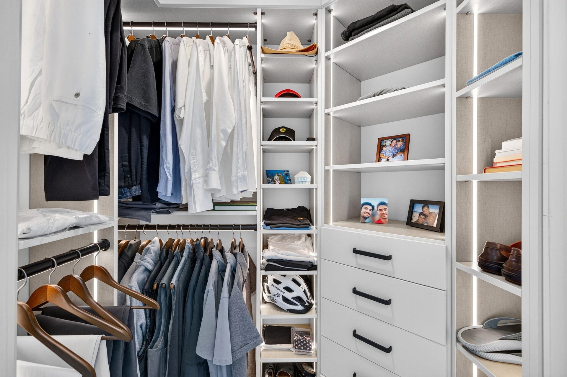 Custom closet system featuring integrated lighting, multiple shelving units, and built-in drawers with black hardware