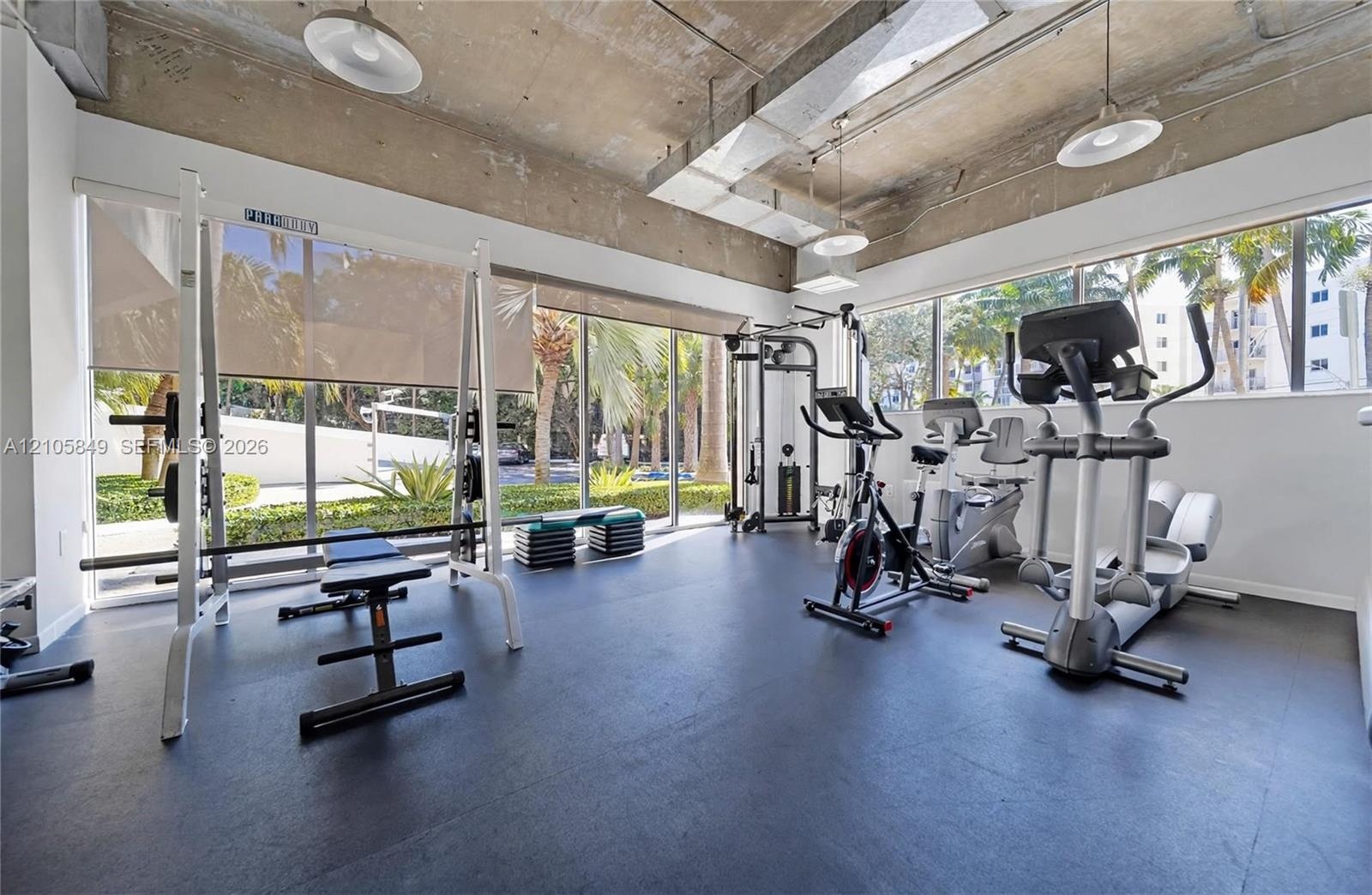 Fitness area featuring exposed concrete ceilings, expansive floor-to-ceiling windows, rubberized flooring, and industrial-style pendant lighting