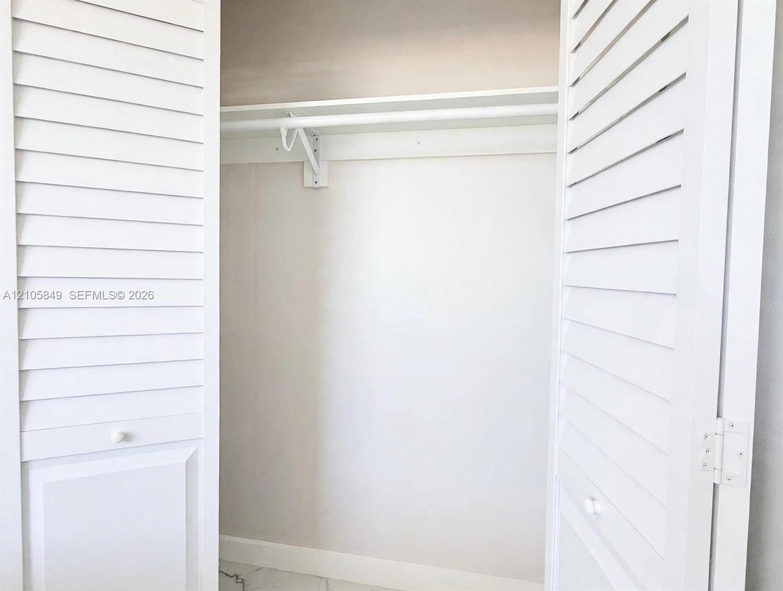 Storage closet featuring white louvered bifold doors and an integrated shelving rod