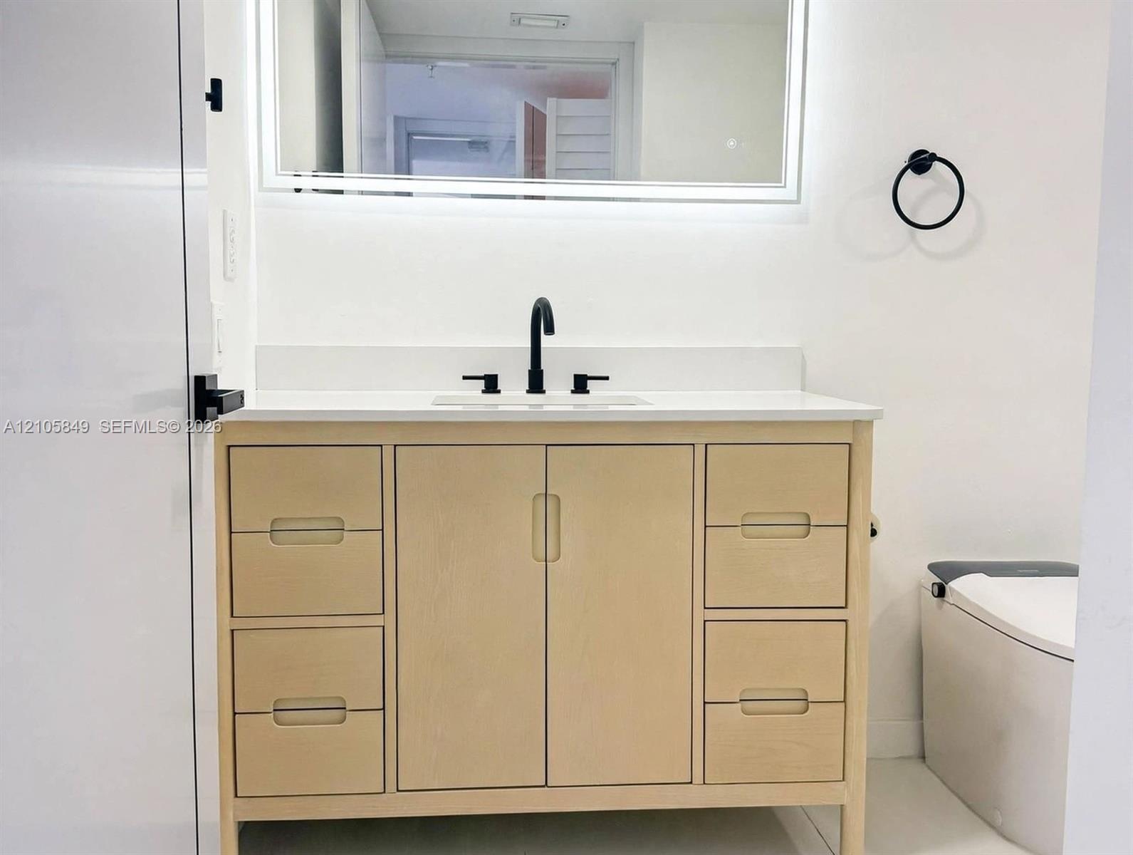 Light-toned wood vanity with integrated storage drawers and cabinets, topped with a solid-surface countertop and undermount sink