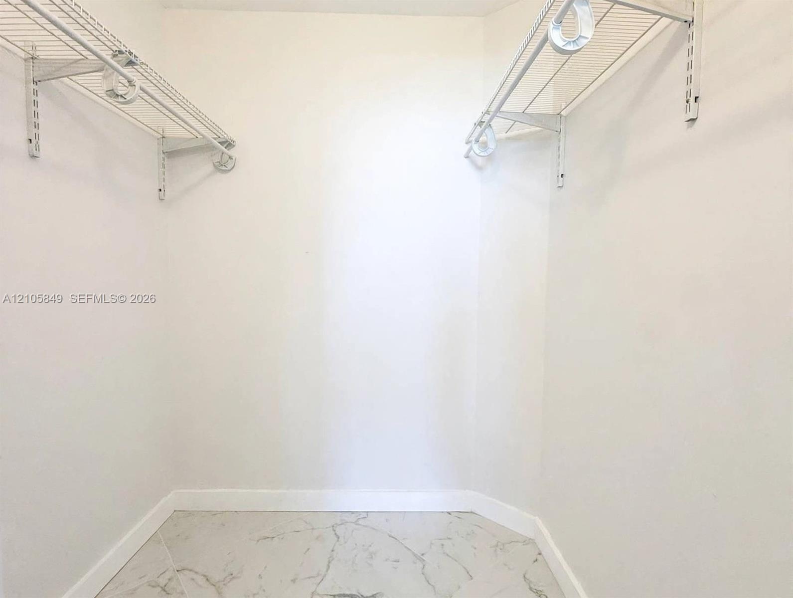 Walk-in storage space featuring white walls and tile flooring with a veined pattern, equipped with dual white wire shelving systems