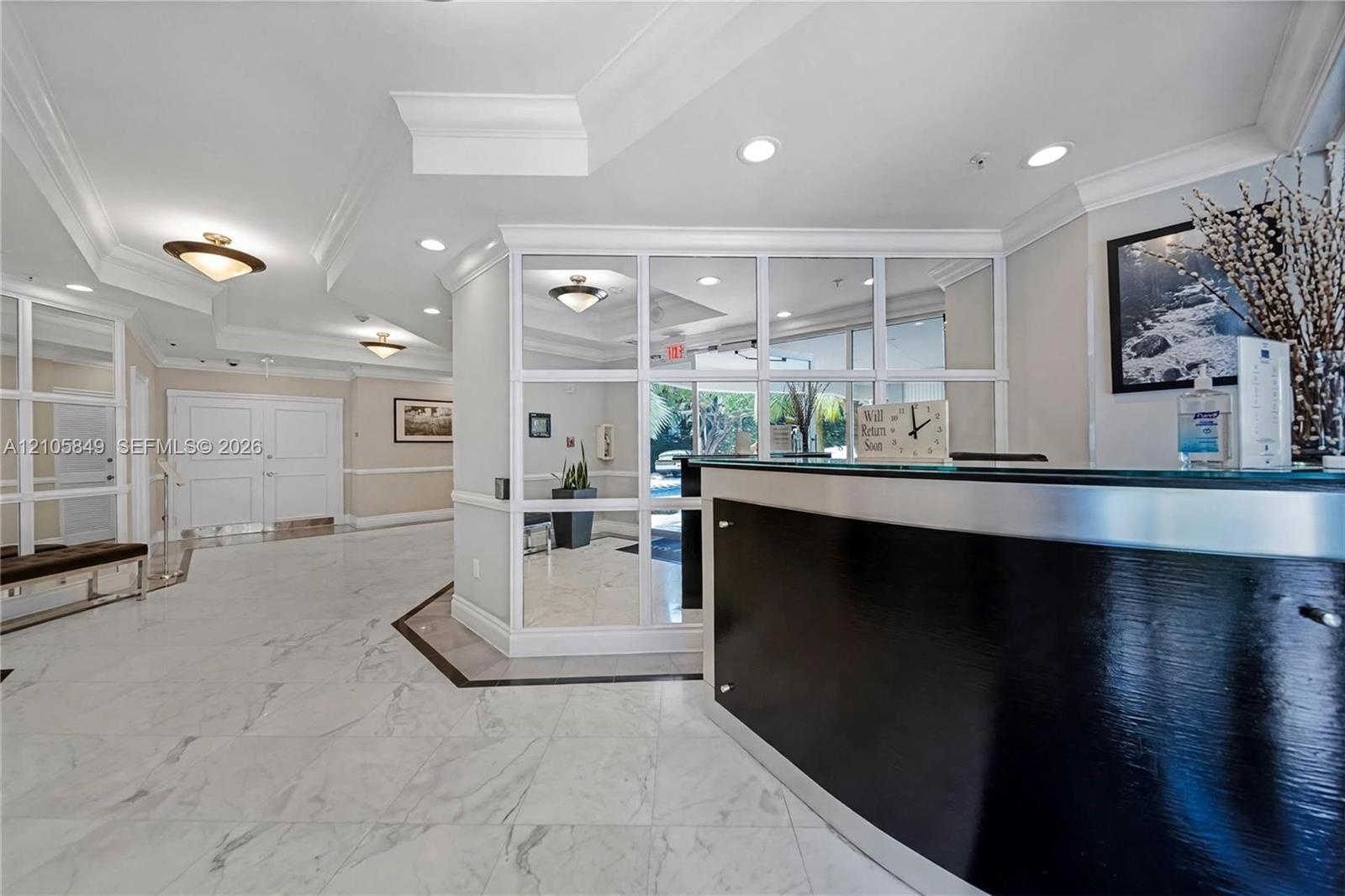 Lobby featuring polished stone flooring, custom grid-patterned glass partitioning, crown molding, recessed lighting, and a built-in reception desk wit