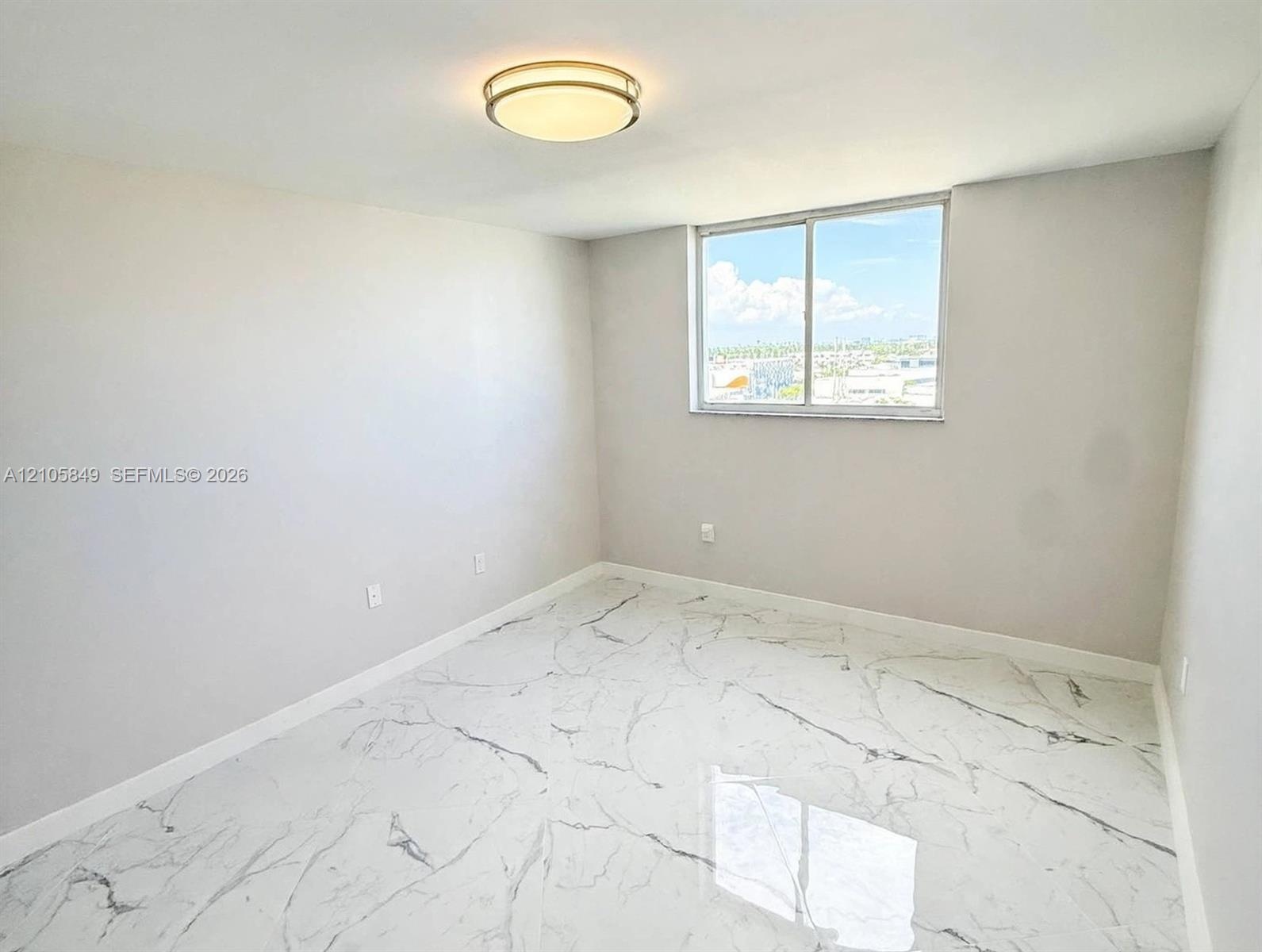 Large-format tile flooring with veined detailing, neutral wall tones, flush-mount ceiling light fixture, and a single sliding window