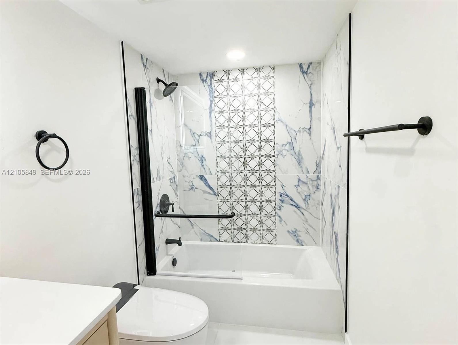 Bathtub with floor-to-ceiling marbled wall tile and decorative geometric tile inlay, complemented by matte black fixtures including a wall-mounted tow