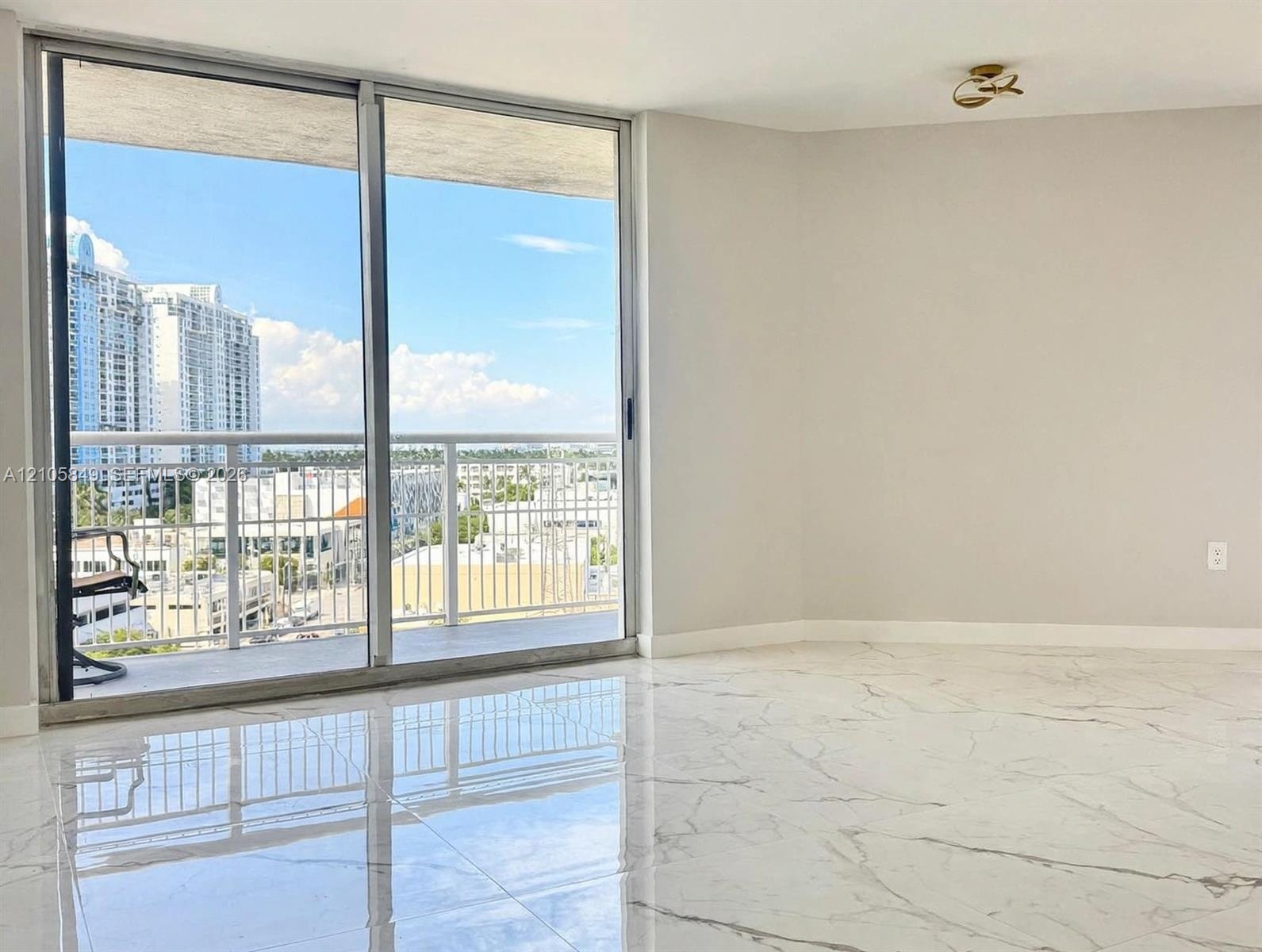 Large-format polished tile flooring, floor-to-ceiling sliding glass doors, and a private balcony with metal railing