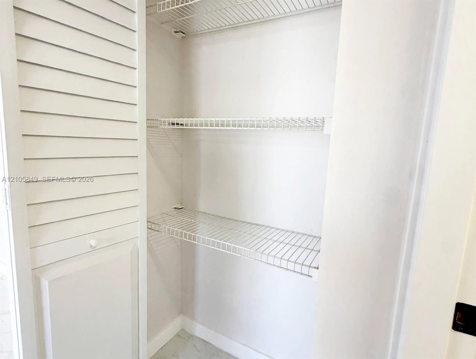 Storage closet featuring white louvered double doors and interior white wire shelving