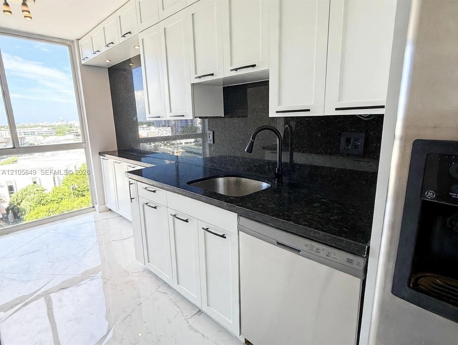 White Shaker cabinetry with matte black hardware, dark stone countertops, full-height stone backsplash, stainless steel undermount sink with a goosene