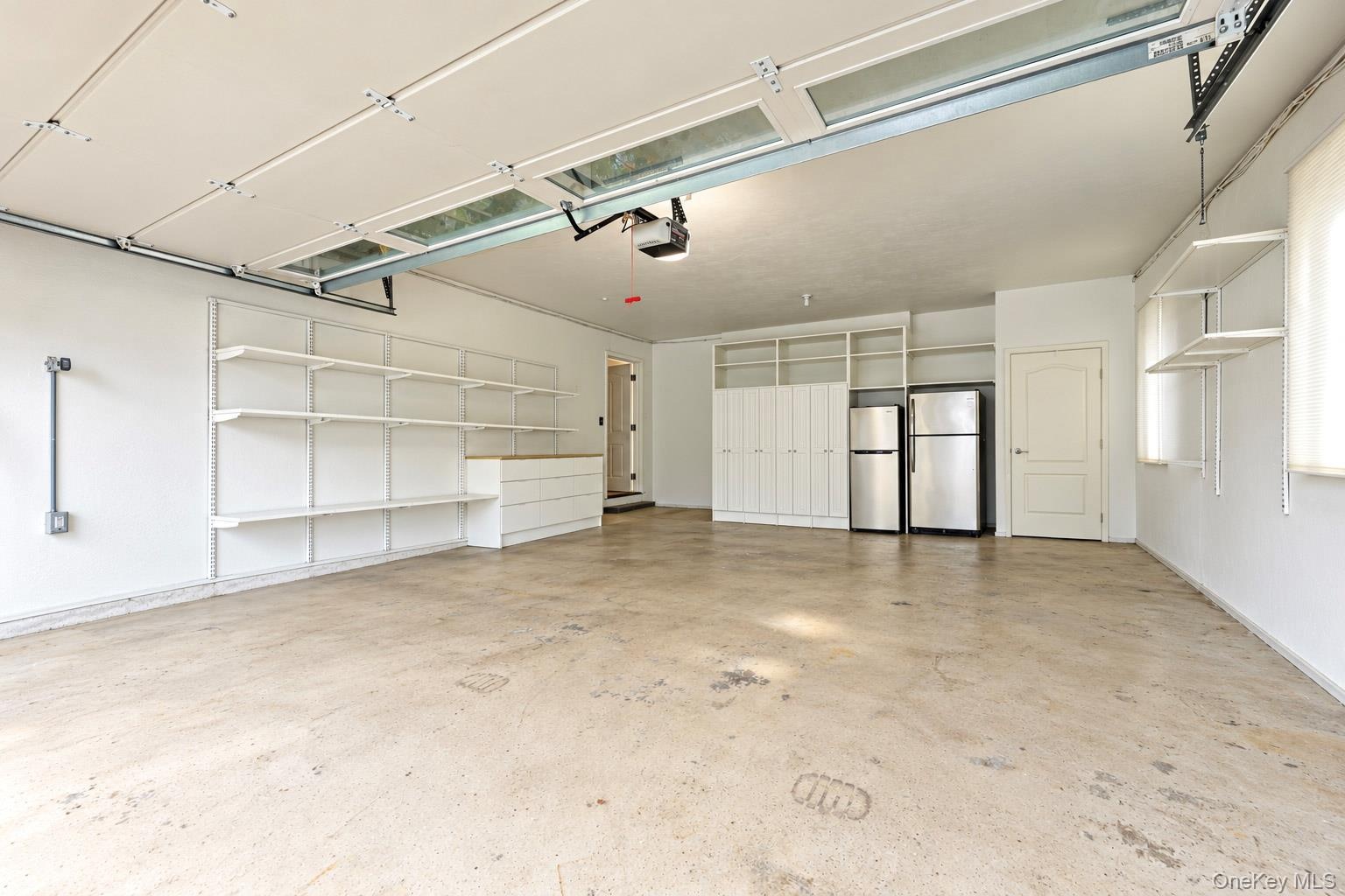 Multi-car garage featuring a concrete floor, integrated wall shelving, built-in cabinetry, and overhead lighting