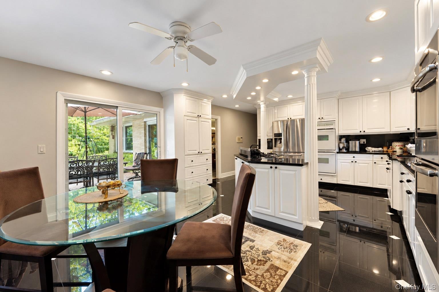 Kitchen featuring white cabinetry, black countertops, recessed lighting, a decorative architectural column, and polished dark tile flooring