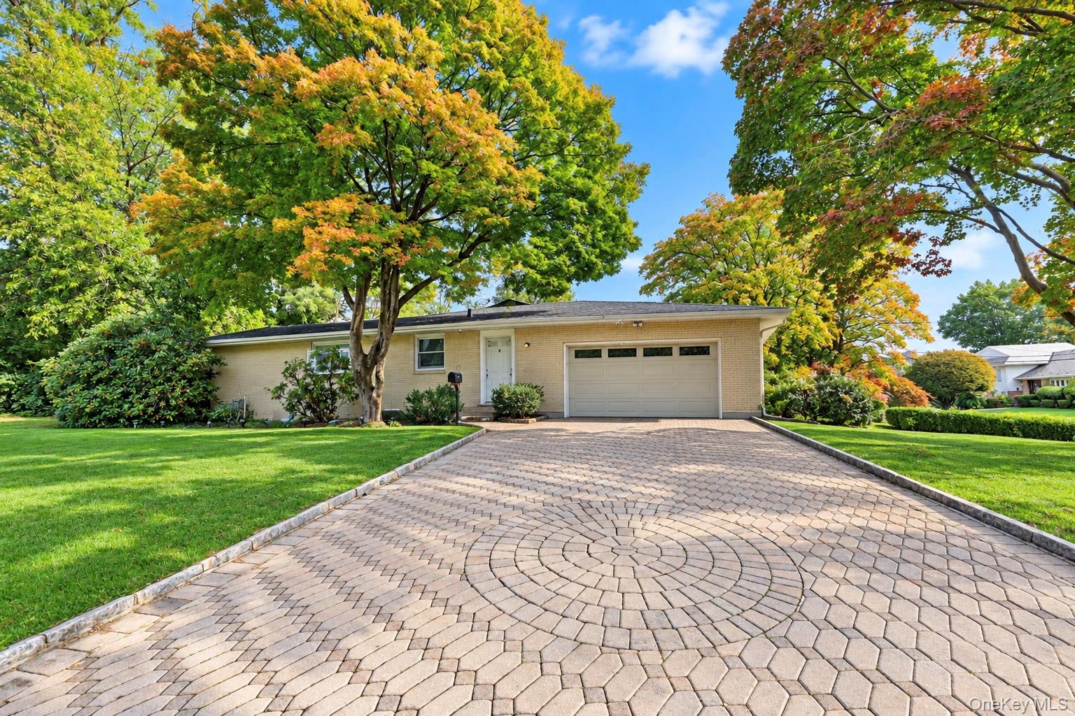 Single-story brick exterior featuring a patterned paver driveway, attached two-car garage, and established landscaping