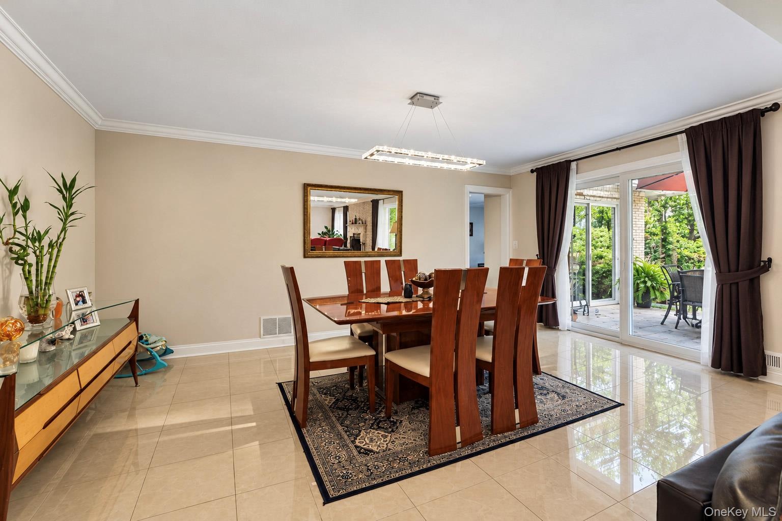 Dining area featuring polished large-format floor tiles, crown molding, a modern linear chandelier, and sliding glass doors to the exterior