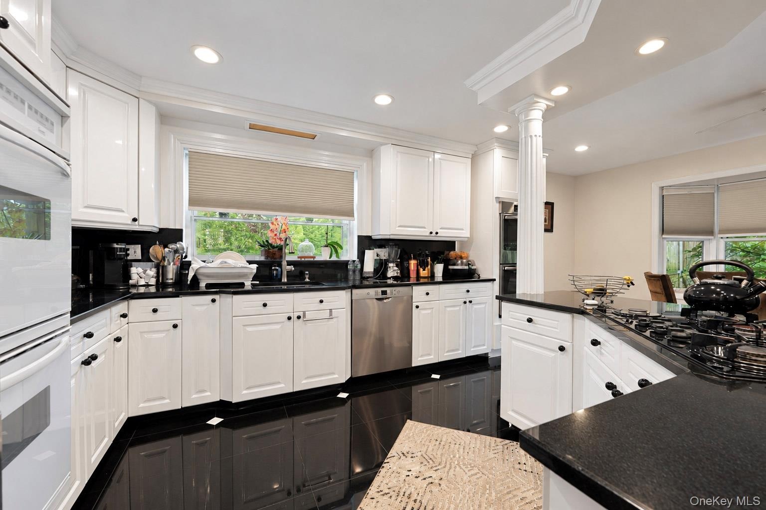 Kitchen featuring white cabinetry, dark stone countertops, stainless steel appliances, recessed ceiling lighting, and a decorative column