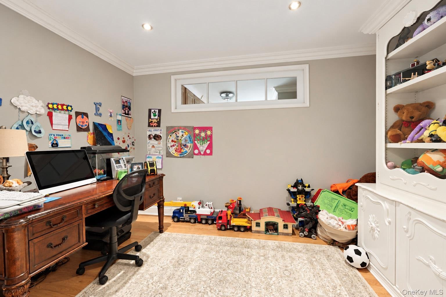 Room featuring wood-finish flooring, built-in white cabinetry with display shelving, crown molding, recessed lighting, and a horizontal transom window