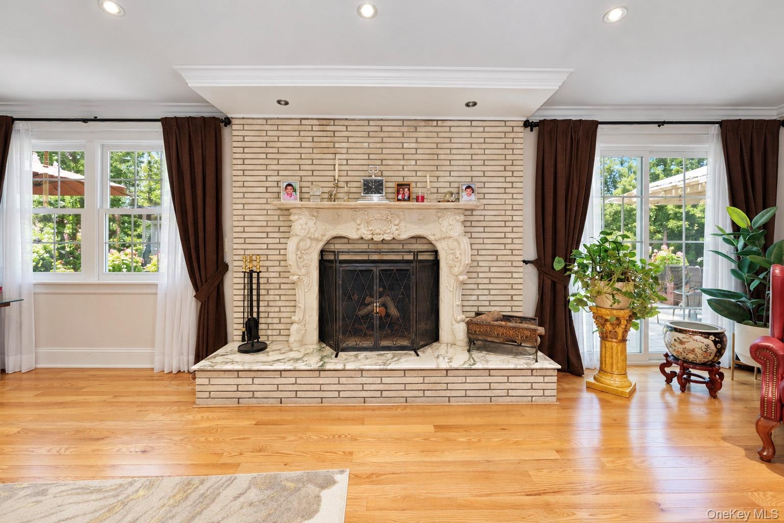Light-toned brick fireplace with an ornate carved mantel and stone hearth, wood-finish flooring, recessed lighting, and glass paneled doors