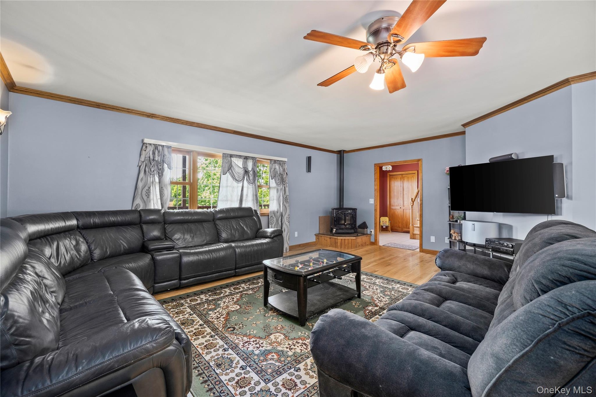 Living area featuring a pellet stove, wood finished floors, ceiling fan, and ornamental molding