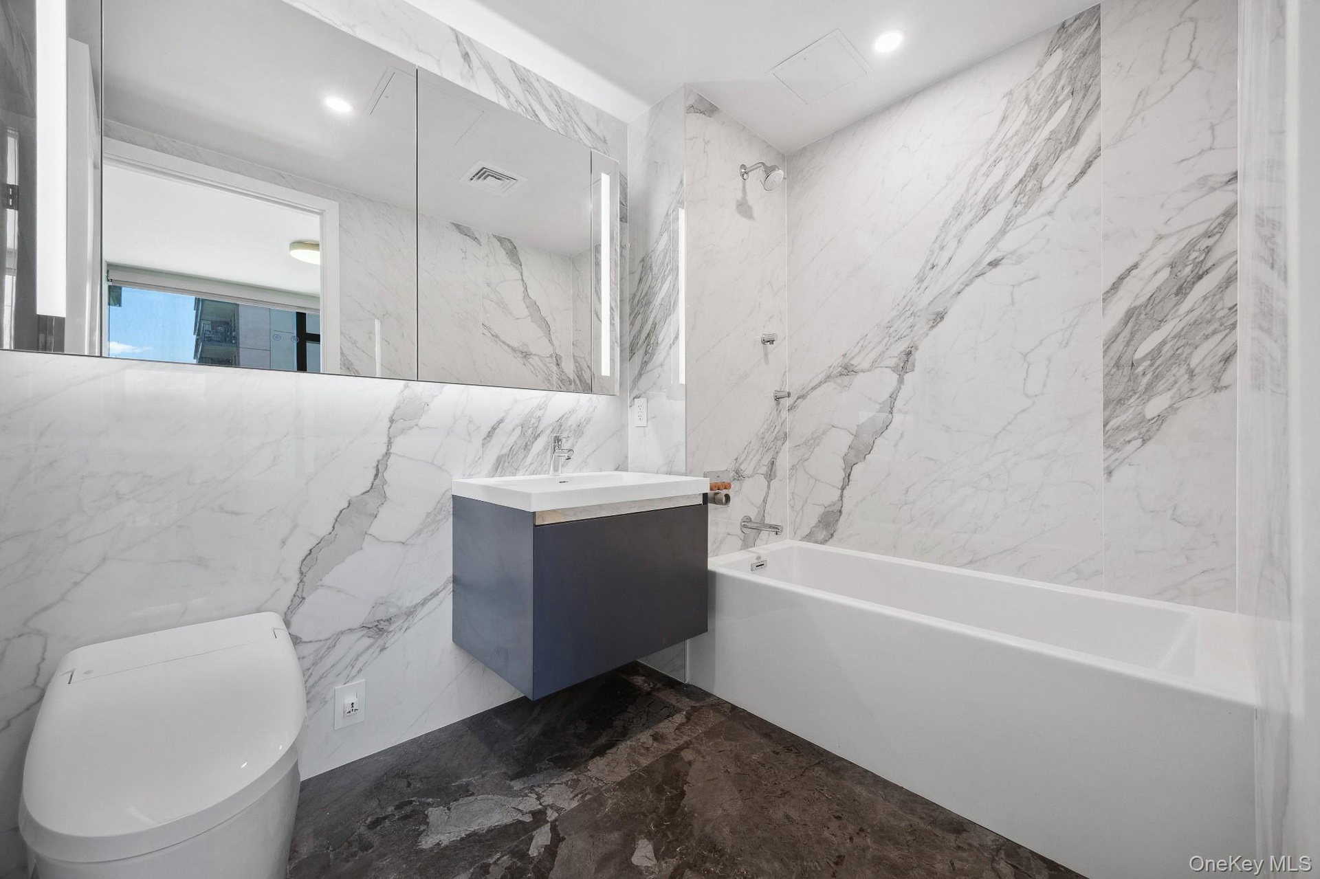 Full bathroom featuring shower / bath combination, marble tiled flooring, vanity, toilet, and tile walls