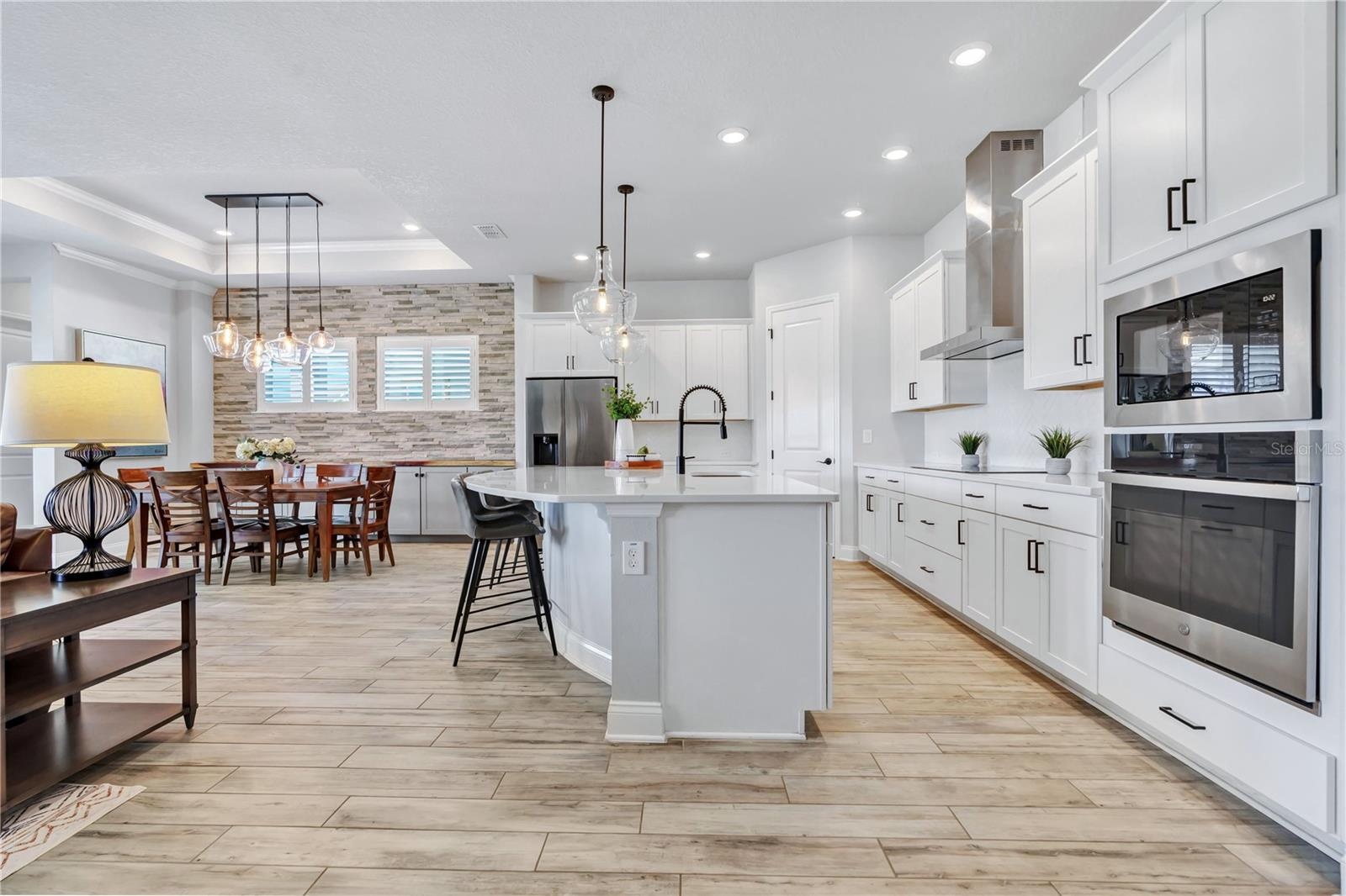 Kitchen view from the great room showing the oversized quartz island, 42 inch cabinetry, wall oven, and microwave.